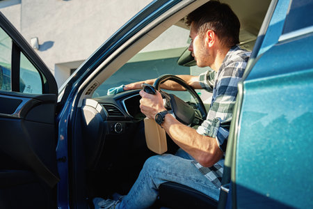 Man cleaning car dashboard with microfiber cloth and spray bottle. Concept of auto interior maintenance, vehicle disinfection and car hygieneの写真素材