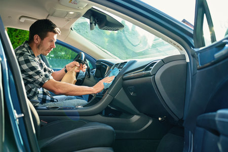 Man cleaning car dashboard with microfiber cloth and spray bottle. Concept of auto interior maintenance, vehicle disinfection and car hygieneの写真素材