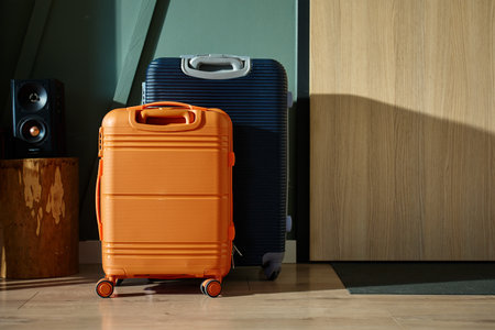 Two modern suitcases, orange and navy, stand near entrance door in morning light. Packed luggage in living room ready for vacation trip. Concept of travel preparationの写真素材