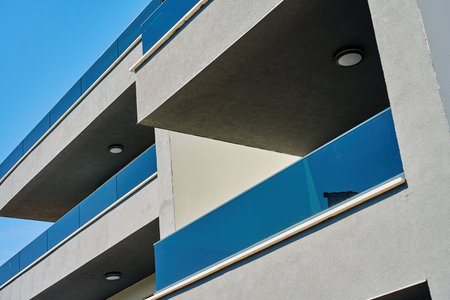 Facade of modern apartment building with minimalist balconies and glass railing under blue sky. Contemporary residential architecture, geometric design and urban housing conceptの写真素材