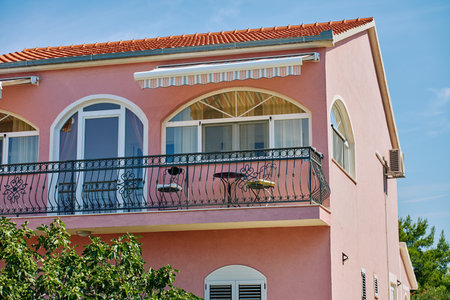 Pink residential house with arched windows and balcony. Villa with balconies and lush greenery. Mediterranean architectureの写真素材