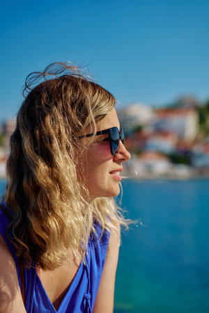 Side view of woman in sunglasses and blue dress looking at the sea on sunny day. Female tourist relaxing by sea. Concept of relaxation, travel and summer vacationの写真素材