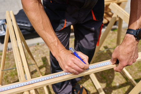 Man measuring wooden board during carpentry work in front of residential building. Concept of...