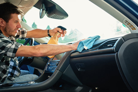 Man cleaning car dashboard with microfiber cloth and spray bottle. Concept of auto interior...
