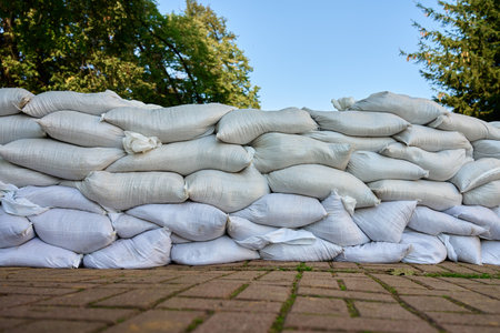 Rows of sandbags stacked as flood barrier on city street. Emergency protection measure to prevent water damage during storms, heavy rain or floodsの写真素材