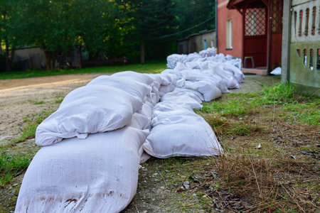 Sandbags stacked outside building to protect against flooding. Emergency flood prevention and natural disaster preparedness concept with protective water barrier near residential house