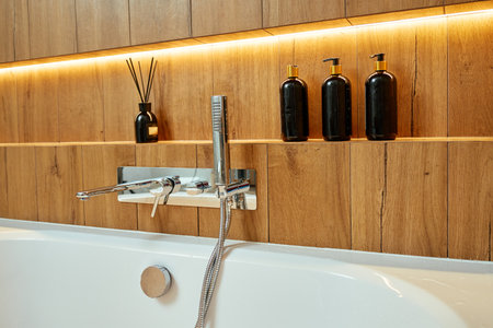 Modern chrome bathtub faucet with shower head mounted on wall with decorative candle and bottles. Contemporary bathroom interiorの写真素材