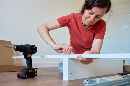 Woman assembling bed frame on wooden floor, using wrench and drill for installation. DIY furniture assembly and home improvementの写真素材