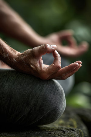 Close-up of hands in meditation pose on crossed legs outdoors with blurred green background. Concept of yoga, mindfulness and relaxationの素材