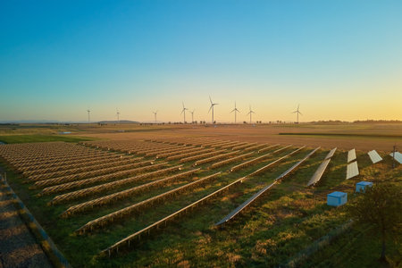 Rows of solar panels and wind turbines in countryside field at sunset. Concept of renewable energy, sustainable technology and clean electricity productionの写真素材