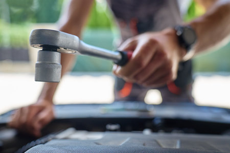 Male mechanic using socket wrench to repair car engine in garage. Man with repair tools in hands under open hoodの写真素材