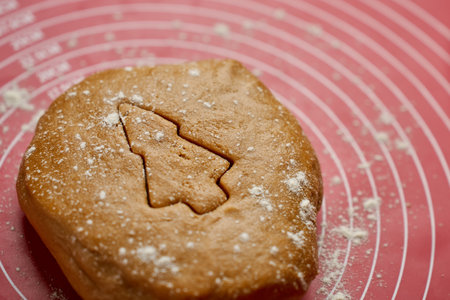 Christmas tree shape cut out in gingerbread dough. Ball of dough dusted with flour on red baking mat, top viewの写真素材