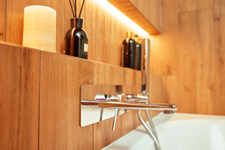 Modern chrome bathtub faucet with shower head mounted on wall with decorative candle and bottles. Contemporary bathroom interiorの写真素材