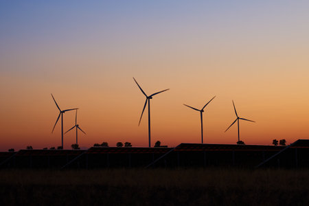 Silhouette of wind turbines and solar panels against colorful sunset sky. Concept of renewable energy, sustainability and green power productionの写真素材