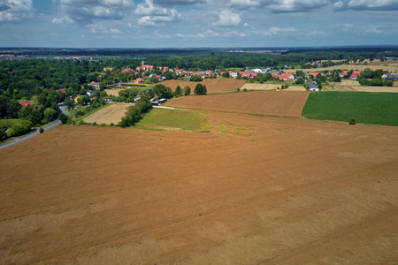 Aerial view of small village surrounded by agricultural fields, forests and farmland under blue skyの写真素材