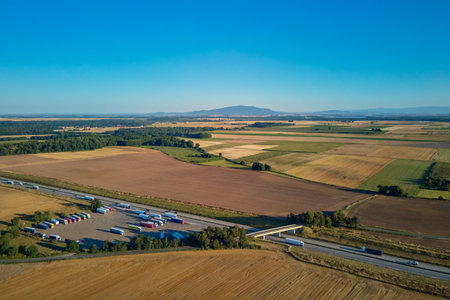 Aerial view of trucks parked at highway rest area surrounded by agricultural fields and mountains in backgroundの写真素材