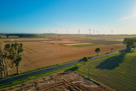 Aerial view of rural road with solar panels and wind turbines in fields at sunset. Concept of renewable energy and countryside landscapeの写真素材