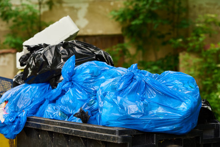 Black and blue plastic garbage bags in large dumpster. Full outdoor garbage containerの写真素材