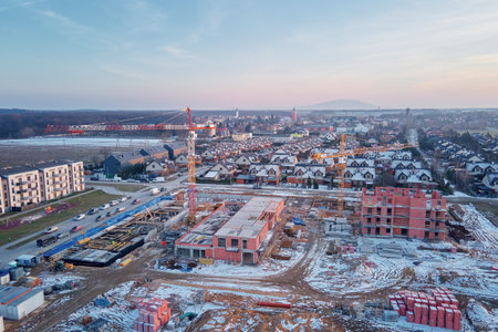 Aerial view of construction site with cranes, unfinished brick buildings and residential houses in background during winter seasonの写真素材