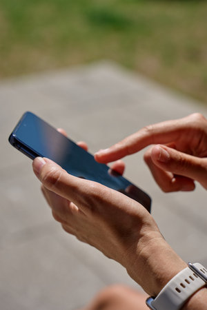 Woman using smartphone. Close-up of female hand holding modern mobile phone outdoors in daylight. Using technology in daily life and communication conceptの写真素材