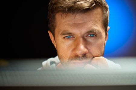 Tired man working at computer in dark room. Close up of man eyes looking at screen. Concept of overworkの写真素材