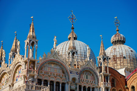Facade and ornate domes of St Mark Basilica in Venice, Italy against clear blue sky. Concept of travel, architecture, history and cultural heritageの写真素材