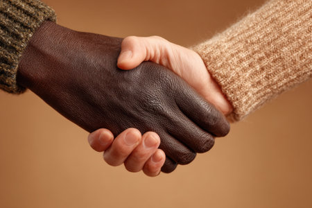 Close-up of handshake between two people with different skin tones against neutral background. People from different ethnics shaking hands. Teamwork and conceptの素材