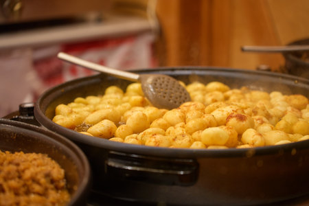 Fried potatoes and traditional stew cooking in large pans at Christmas market. Street food stall at festive fair at night. Concept of winter holidays in European cityの写真素材