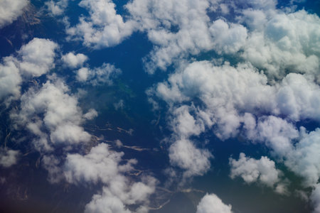 Aerial view from airplane window of white fluffy clouds floating above landscape, with mountains and riversの写真素材