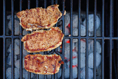 Top view of meat steaks with grill marks grilling on barbecue over hot charcoal briquettes. Concept of outdoor cooking and summer picnicの写真素材