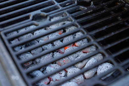 Close-up of hot charcoal briquettes glowing under grate in barbecue grill ready for cooking. Summer grilling, outdoor activity and picnic preparation conceptの写真素材