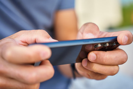 Man using smartphone, close up. Male hands holding smartphone and playing mobile game outdoors. Concept of technology, digital entertainment and gadget usingの写真素材