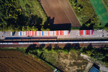 Aerial view of freight train and stacked shipping containers along railway station in rural area. Concept of logistics, transportation and cargo infrastructureの写真素材
