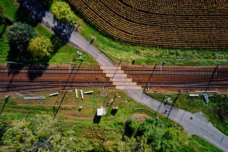Aerial view of railway tracks crossing rural road surrounded by fields and trees. Concept of...