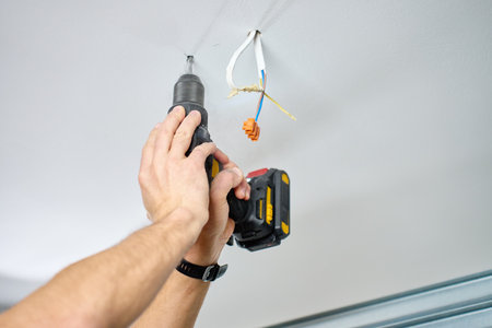 Man wearing work overalls drills hole in ceiling using cordless power drill in indoor room. Concept...