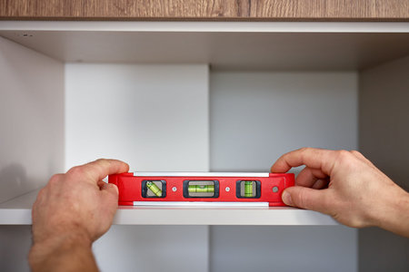 Close up of hands placing spirit level on cabinet shelf inside kitchen cabinet. Using bubble level...