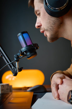 Man wearing headphones speaks into desktop microphone on boom arm near laptop and notebook. Concept...