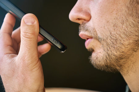 Close up of man speaking to smartphone during voice assistant interaction. Concept of speech recognition, digital communication, everyday AI use and human connection with technology.