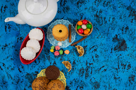 Plate with sweet turnovers and teapot on blue table background. High quality photo