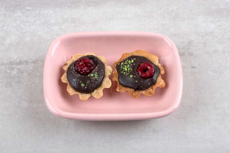 Pink bowl of delicious frosted chocolate cupcakes on stone background. High quality photo