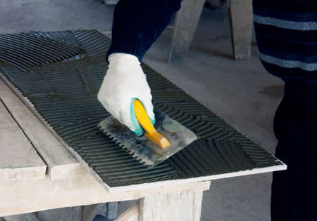 Close up of a builder, a tiler sitting in a glue spreading on a tile.の写真素材