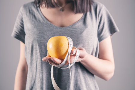 girl holding a centimeter and an apple in her handの写真素材