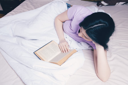 young girl reading a book in bedの写真素材