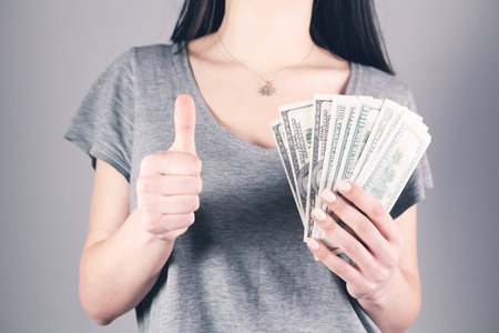the girl holds money in her hands and shows her thumb to the topの写真素材
