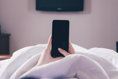 the girl lies in bed and uses the phone