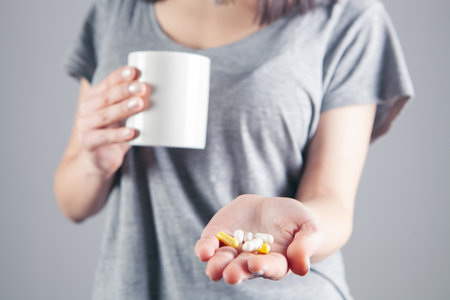 Woman holding pill and glass of water in hands taking emergency medicineの写真素材