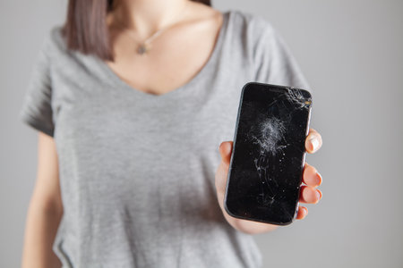 young girl showing broken phone screen on gray background