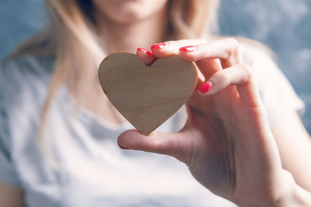 young woman holding wooden heart on gray backgroundの写真素材