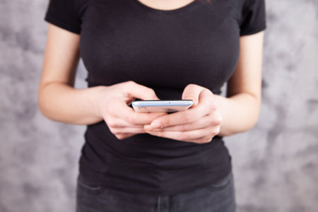 a young woman stands holding a phone in her hand on a gray background