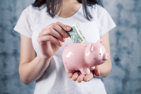 woman throws dollar into piggy bank on gray backgroundの写真素材